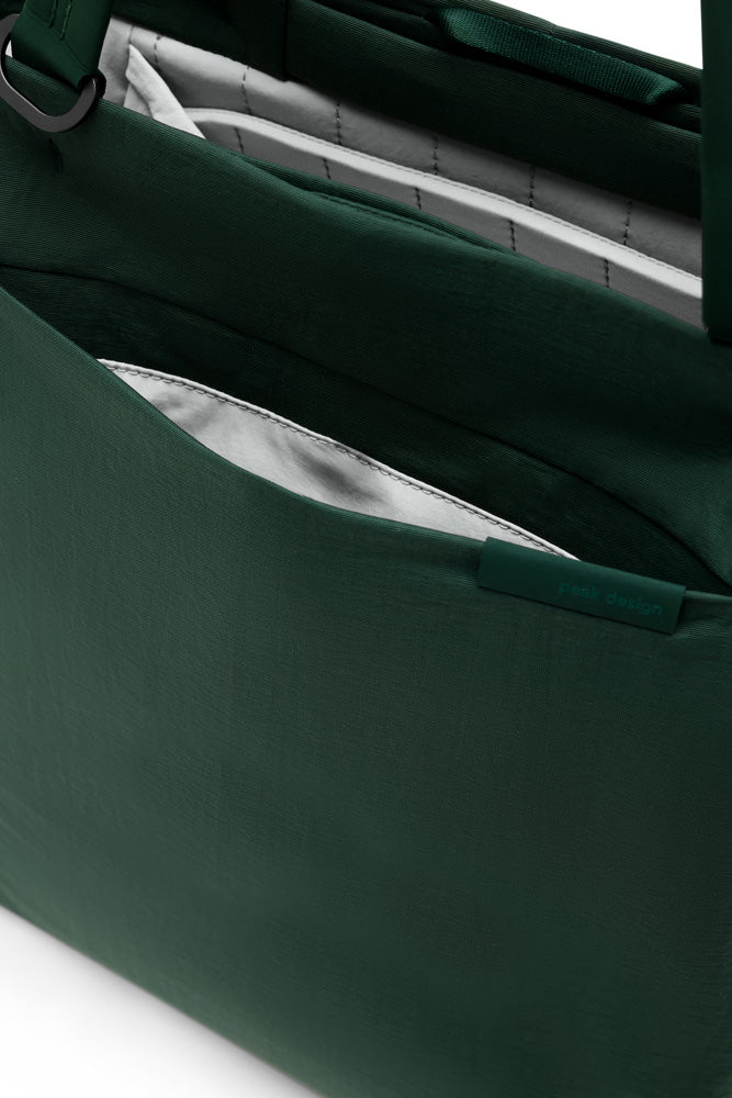 Close-up of a dark green fabric bag showing the interior lining and a side pocket with a matching green tab closure.