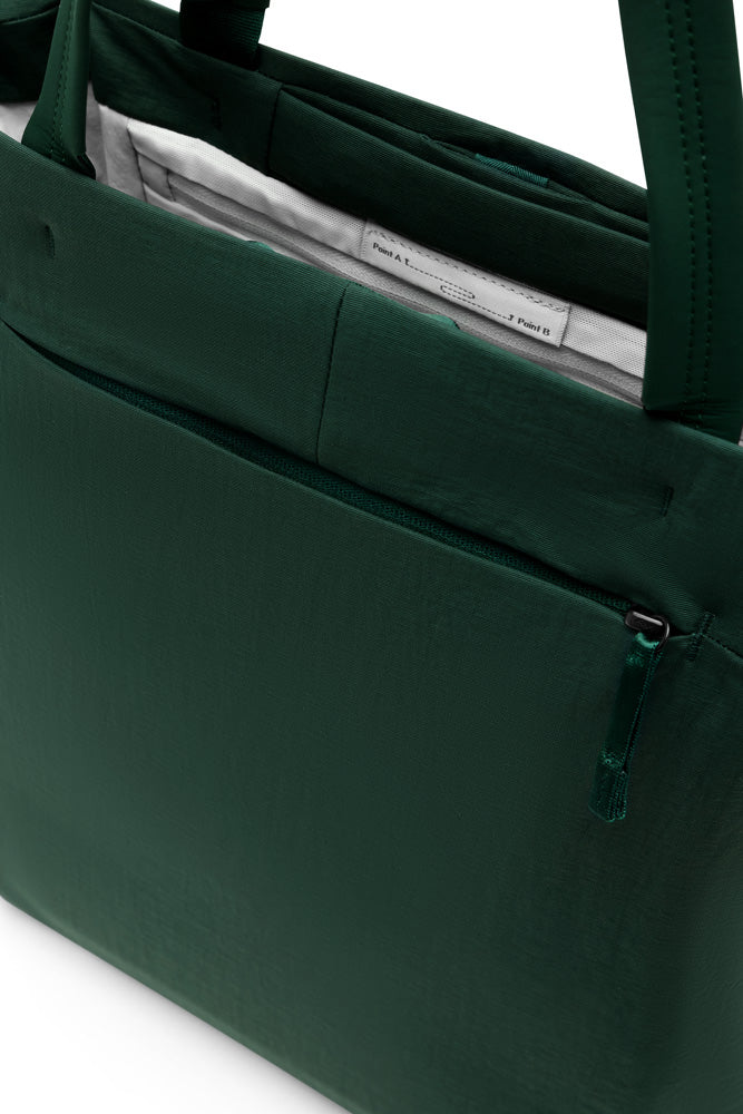 Close-up of a dark green fabric tote bag with a zippered pocket and top handles, showing a light-colored interior lining.