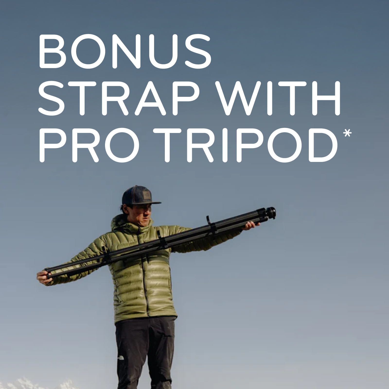 A man standing outdoors on a mountain ridge holds a tripod extended across his arms. Large white text at the top reads 'BONUS STRAP WITH PRO TRIPOD*', and a small Pro Tripod logo appears near the bottom right.