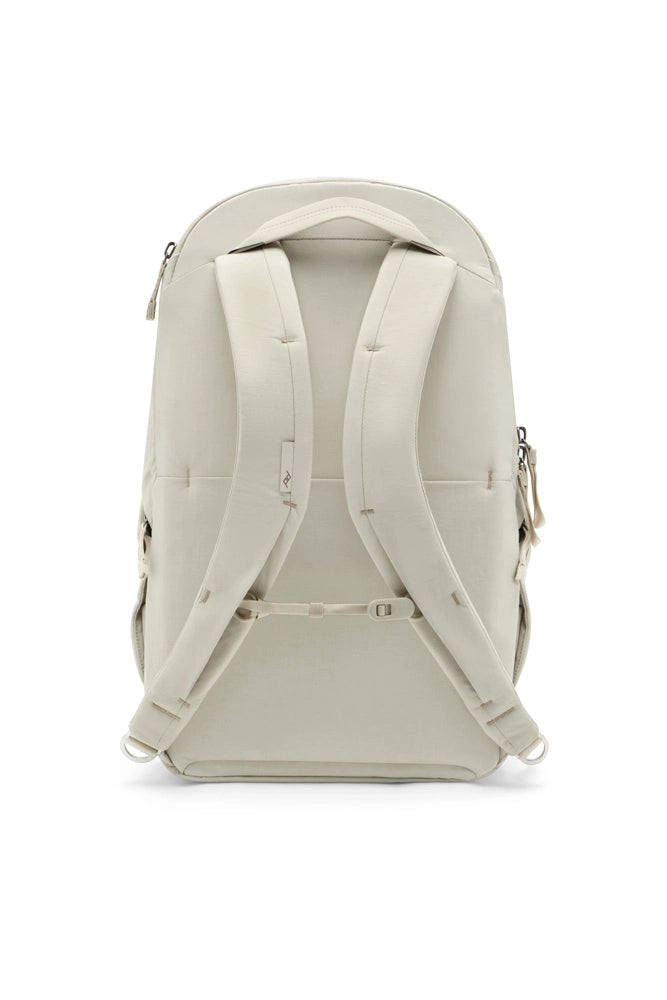 A light beige backpack shown from the back, featuring padded shoulder straps, a top carry handle, and side zipper pulls, photographed against a clean white background.