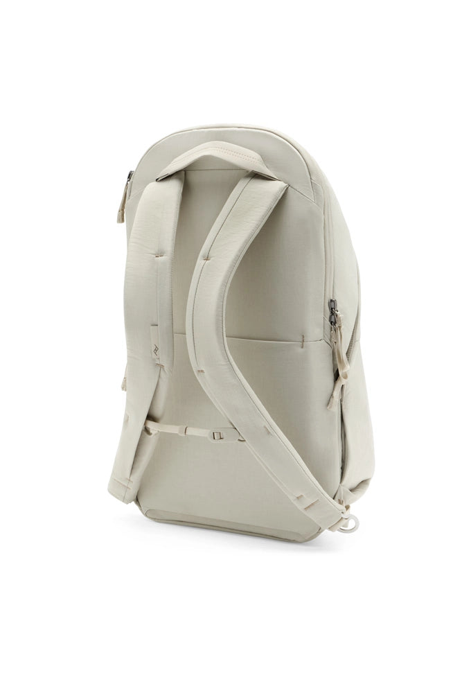 A light beige backpack shown from the back view, featuring padded shoulder straps, a top carry handle, and a zippered main compartment, set against a plain white background.
