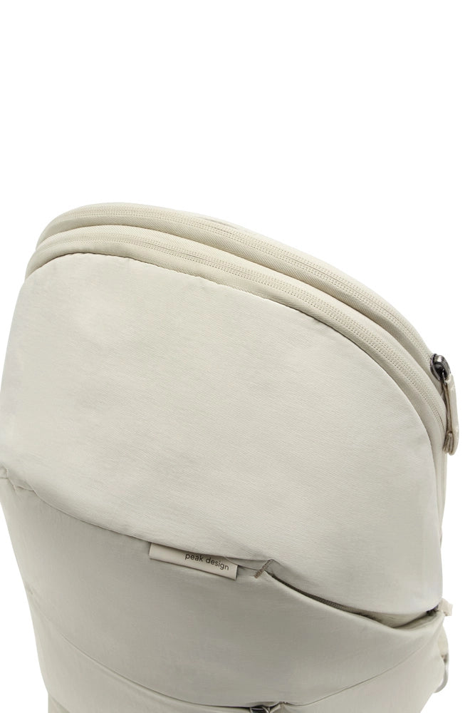 Close-up of a light beige or off-white fabric pouch with a curved zipper and a small visible 'peak design' label near the bottom.