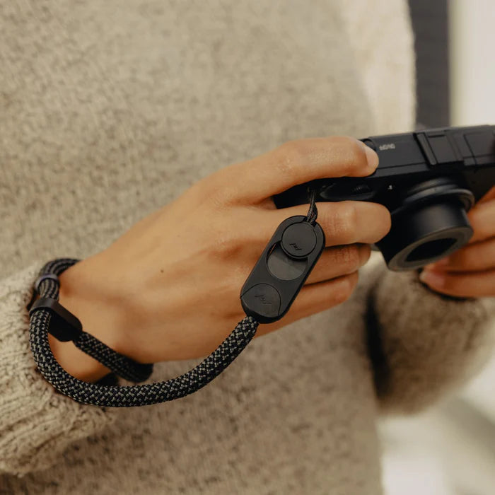 Person holding a camera with a black wrist strap on a blurred background