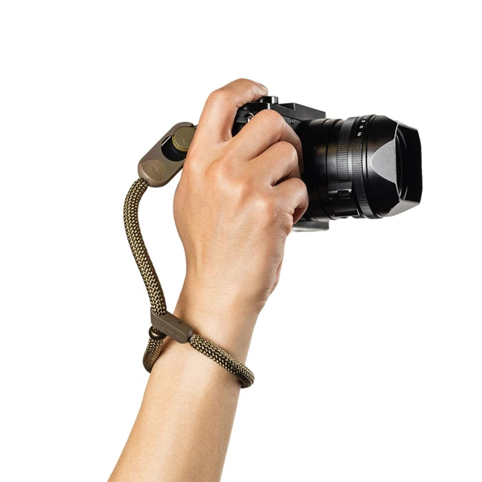 Hand holding a camera with a brown-green strap on a white background