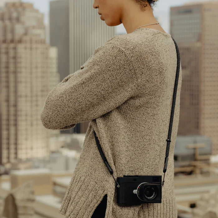 Person wearing a beige sweater with a black camera slung over their shoulder, standing in an urban setting.
