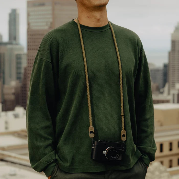 Person wearing a green sweatshirt with a camera around their neck against an urban background