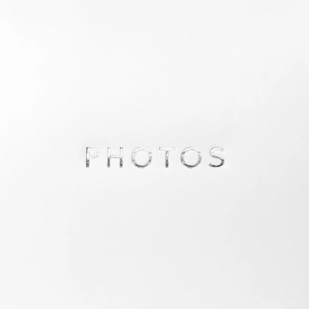 The word 'PHOTOS' is centered on a plain white background in a metallic silver, textured font.