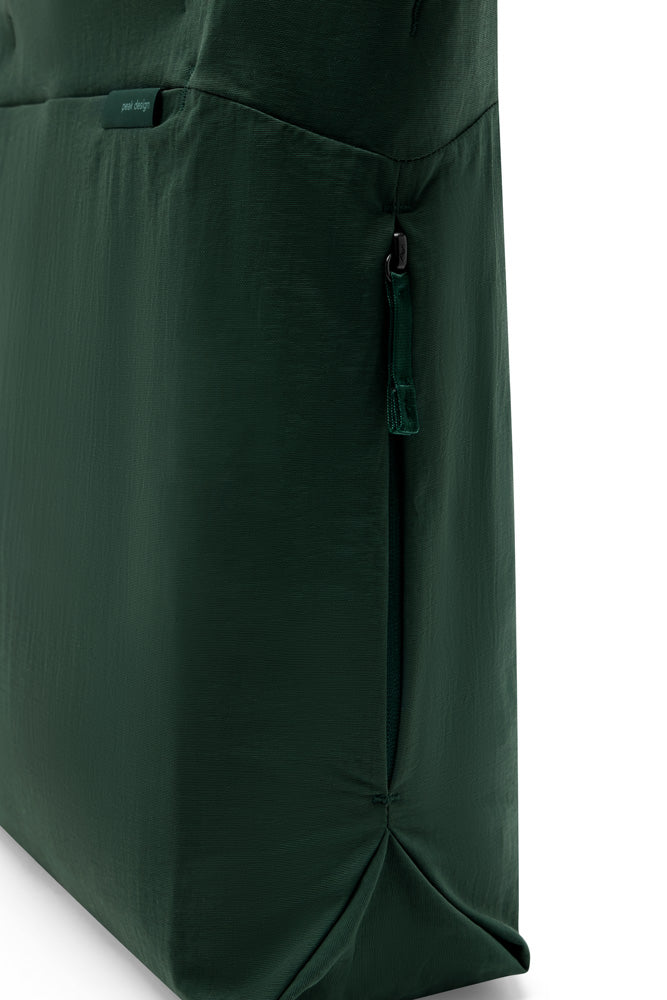Close-up of a dark forest green fabric item, showing a side pocket with a matching green zipper pull and a small fabric brand tag.