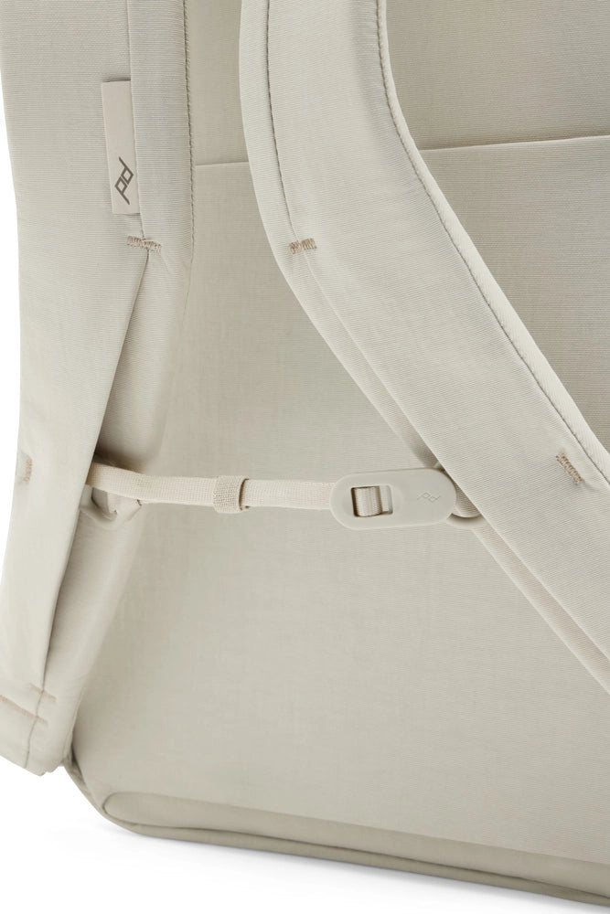 Close-up of a light beige fabric backpack showing the side pocket, strap attachment, and padded edge details.