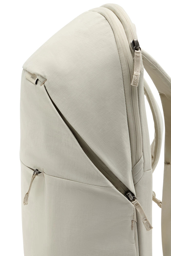 Close-up of a light beige backpack showing the upper portion, front zippered pocket, and side pocket details against a white background.