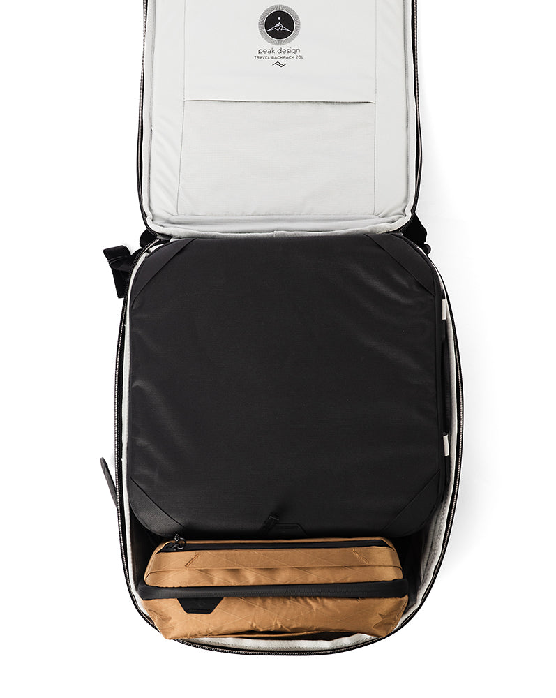 Open large suitcase with black packing cube and brown case packed in on a white background