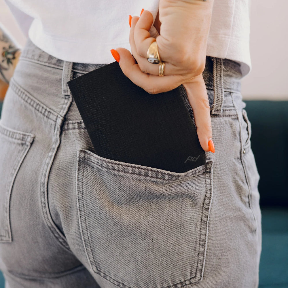 Person inserting a black wallet into their jeans' back pocket