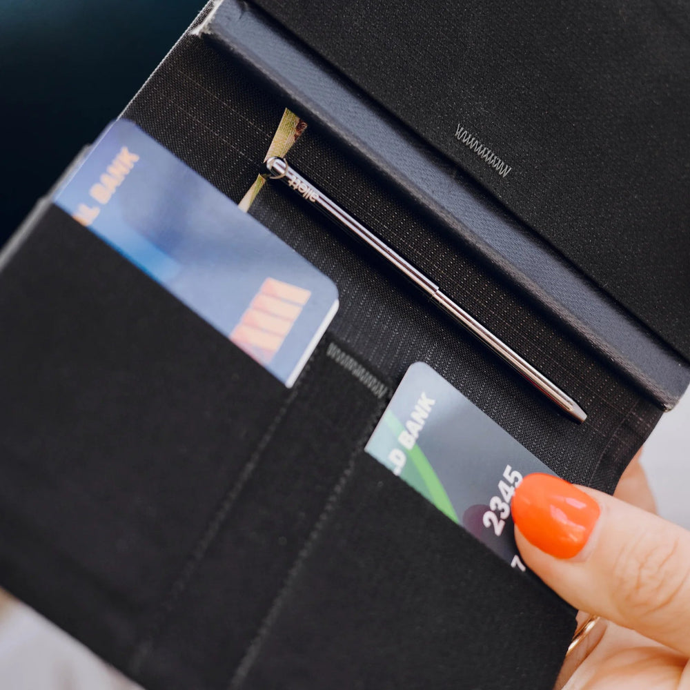 Black wallet with cards and a pen held by a hand with orange nail polish.