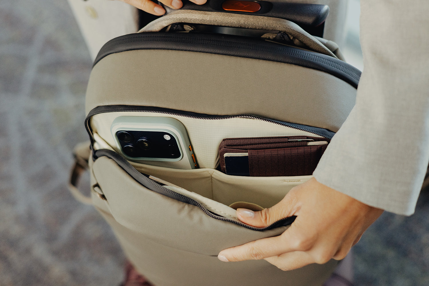 Close-up of a beige suitcase with a phone and wallet inside, held by a person.