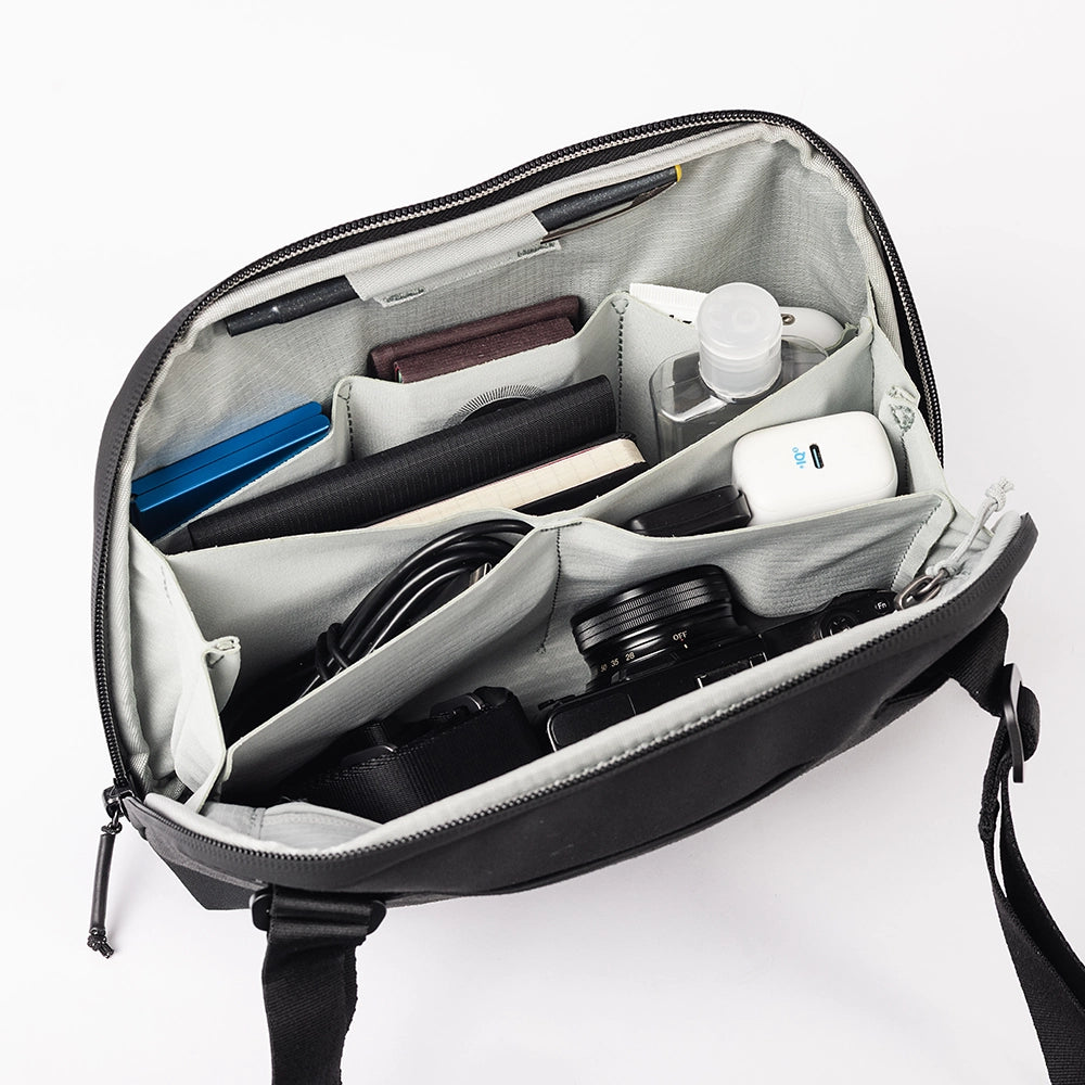 Open black bag with compartments containing various items on a white background