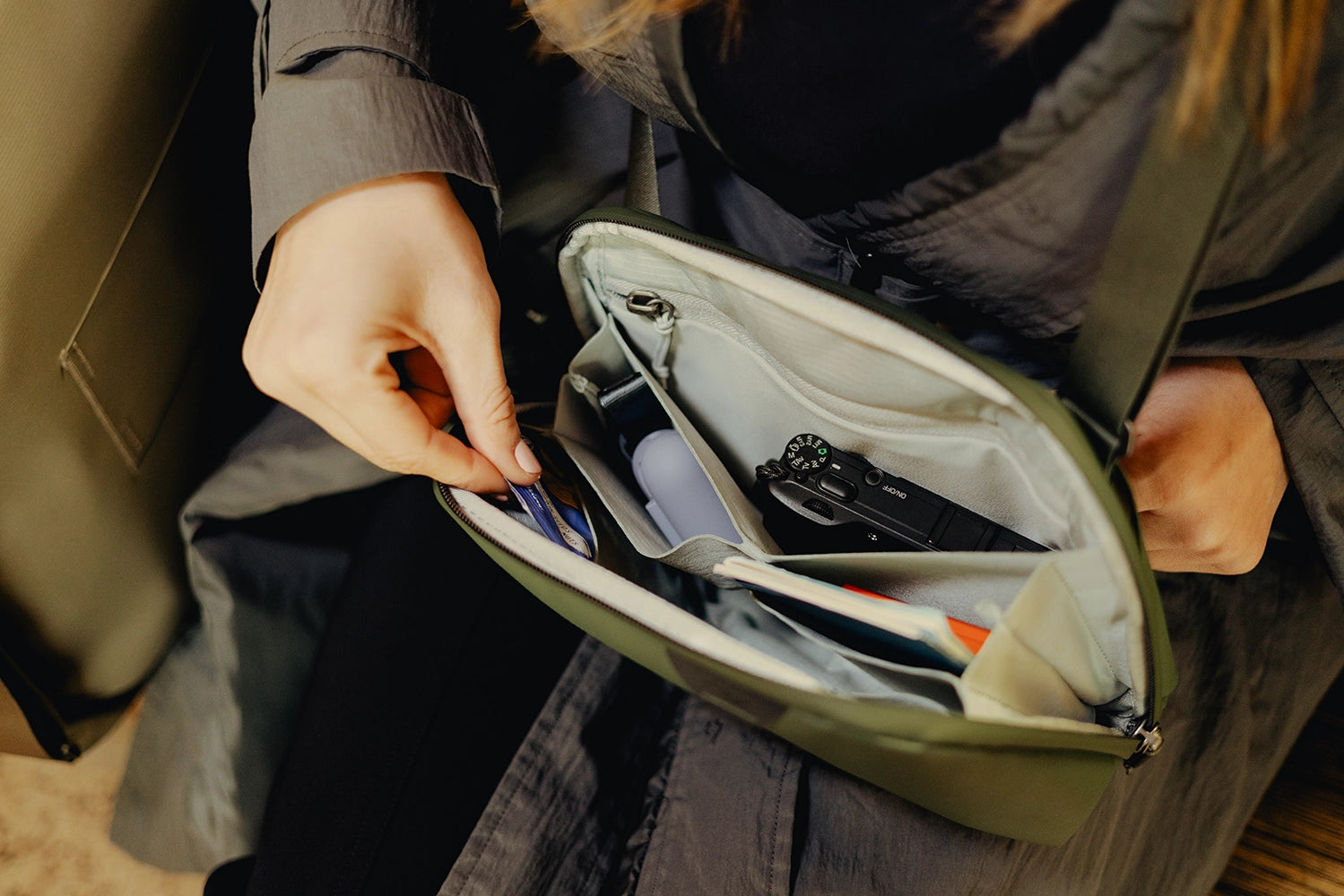 Person opening a green bag to reveal compact camera and other stuff in it.